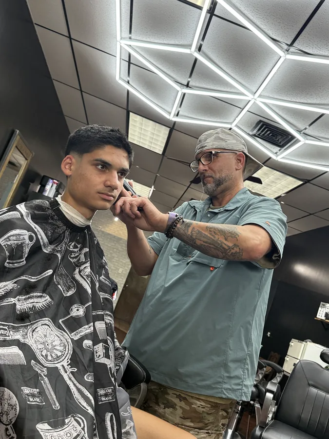 A Blended barber lining up a client's hairline with a trimmer under the hex lights