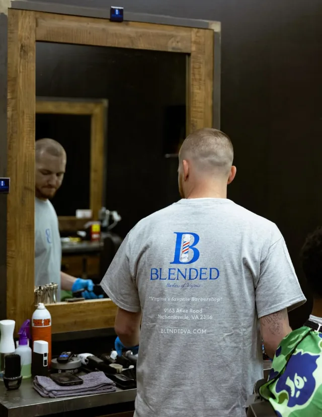 A client in a Blended Barbers shirt seated at the shop mirror