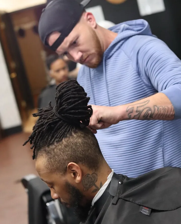 Jerm detailing a client's tied locs and faded sides